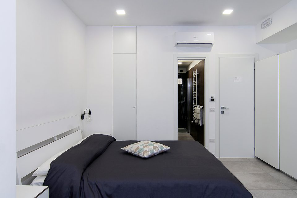 Lit double avec couvre-lit foncé et accès à la salle de bains.